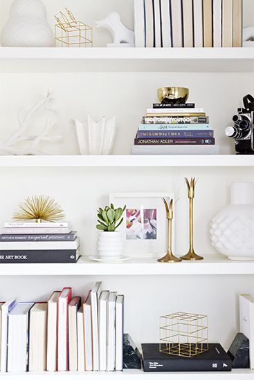 White bookshelf styled with stacks of books, candlesticks, and matching white vases
