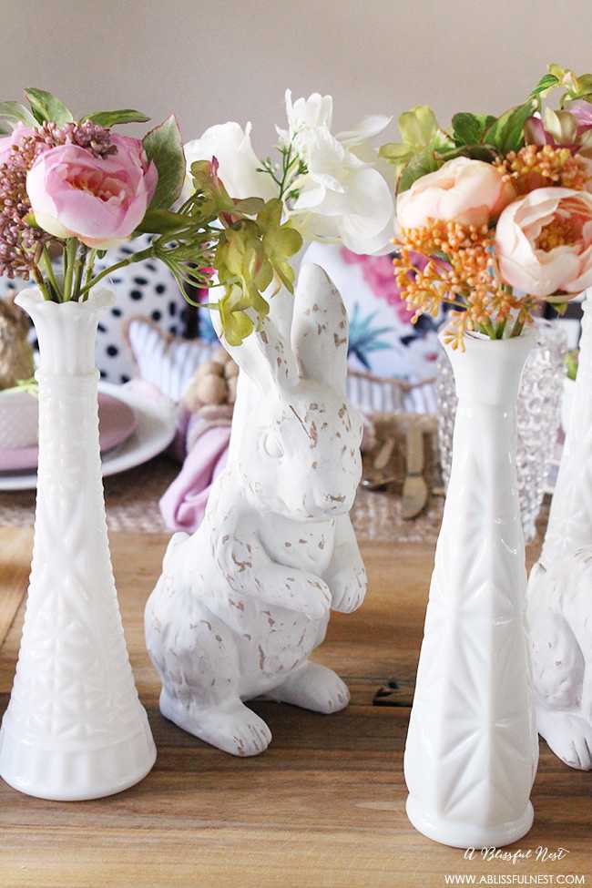 A beautiful and soft Easter table decor setting that is the perfect transition into spring. Soft whites with pops of flowers and pastels makes this Easter table setting perfect for your family! Check out more of this table on ablissfulnest.com