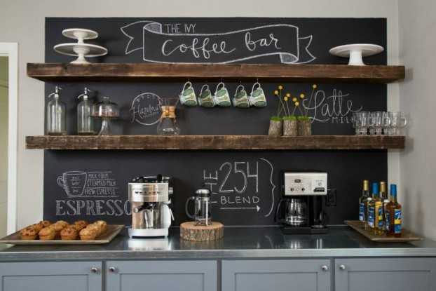 Large chalkboard behind two floating wood shelves with a grey sideboard with a coffee maker.