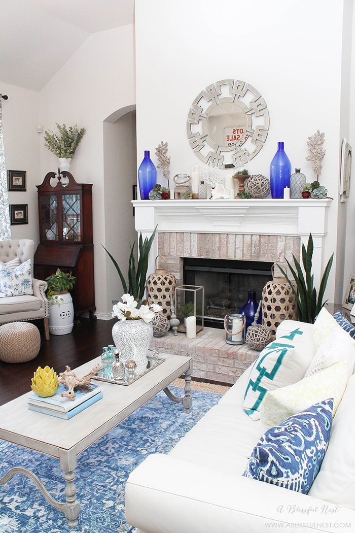If you love the coastal look then this one is for you! Touches of coral, blue and white and gorgeous wood textures were used to create this show stopping fireplace mantle by A Blissful Nest. See more on https://ablissfulnest.com #coastal #livingroom #blueandwhite #coastalliving #livingroomideas #fireplacemantleideas #designtips