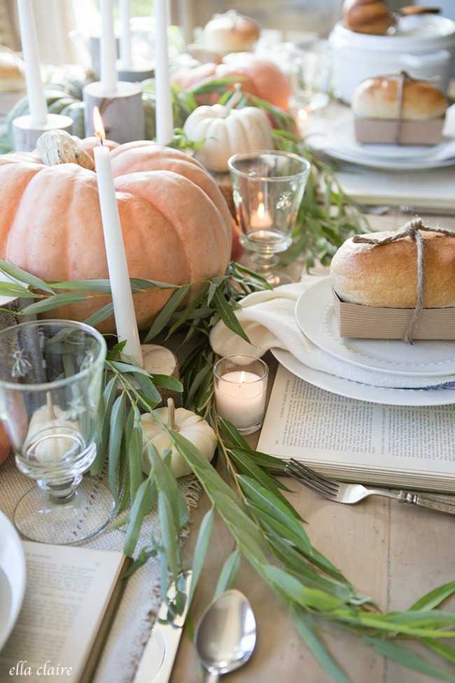 A classic Thanksgiving table with orange and white pumpkins for a centerpiece. Delicious homemade bread is placed on each place setting for guests. Votive tea lights and vintage books are nestled for ambience. 