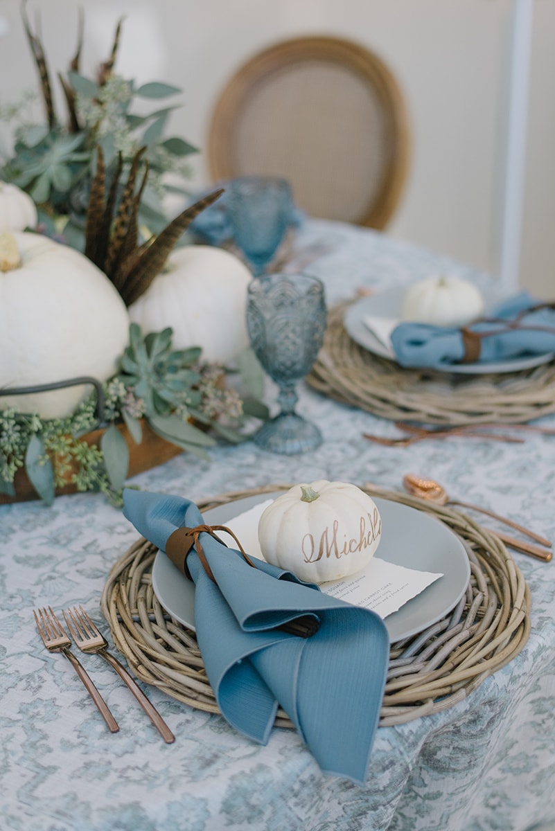 Woven placemats with beautiful light blue plates. White pumpkins with greenery for the middle of the table. Blue crystal glasses tie in the color scheme.