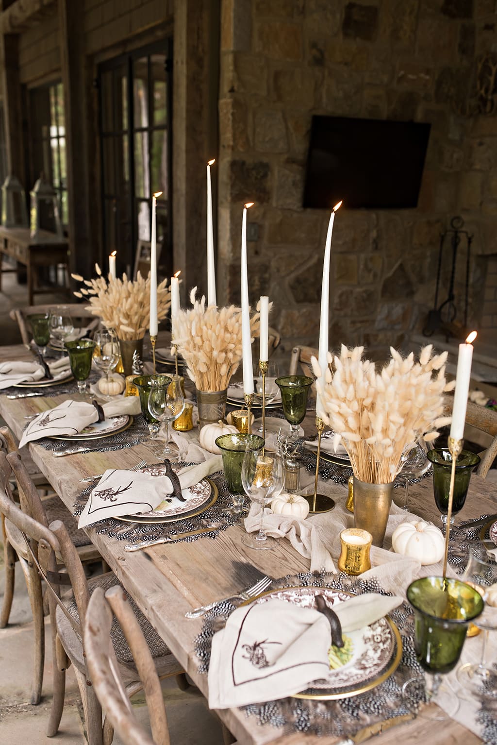 A rustic looking Thanksgiving table with clusters of wheat tied with ribbons for the center of the table with tapered candles. Light green accents with pheasant feathers as placemats.