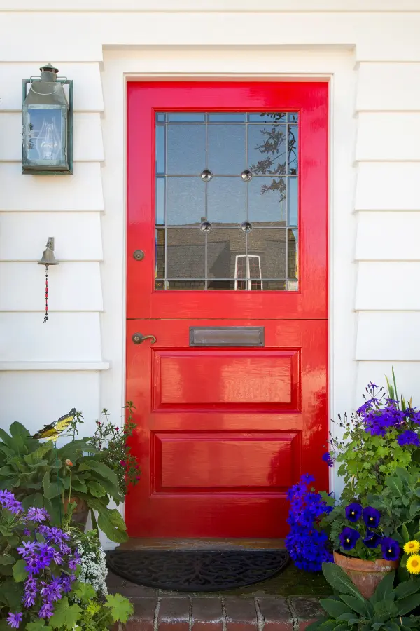 Red front door with purple pansies in planters.