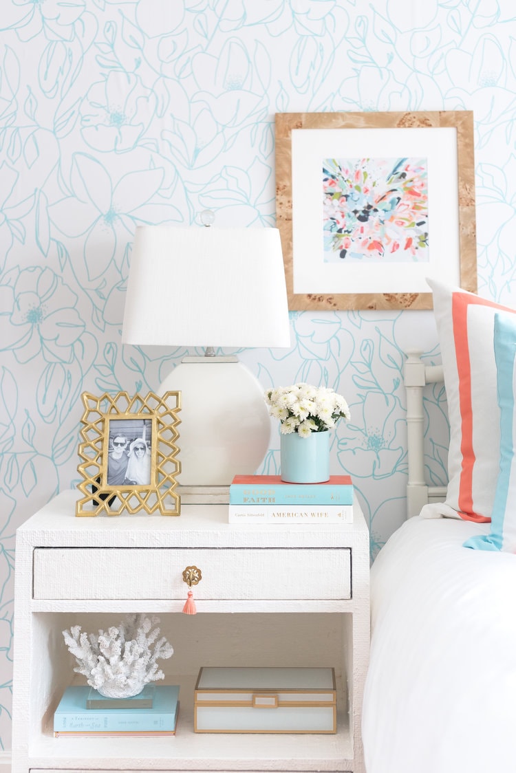 Coral and turquoise bedroom with a floral wallpaper, white nightstand and gold picture frame. 