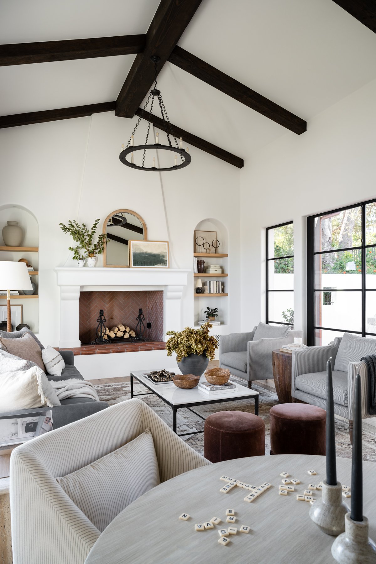 modern transitional living room with a mirror and artwork layered on a fireplace mantel with 2 white vases and greenery