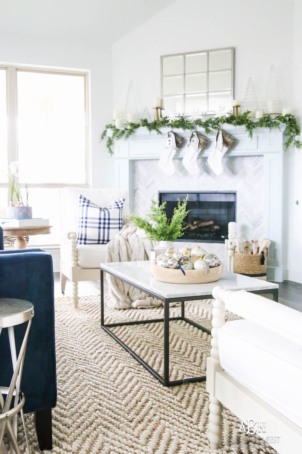 Gorgeous blue and silver Christmas mantle décor with juniper berry garland and glass hurricane Christmas trees. Simple and festive holiday décor in this open concept living space. Check out all the white, silver and gold Christmas decor in this holiday home tour on ABlissfulNest.com. #ABlissfulNest #Christmasdecor #Christmasdecorating #CoastalChristmasdecor #christmastree #christmasmantle