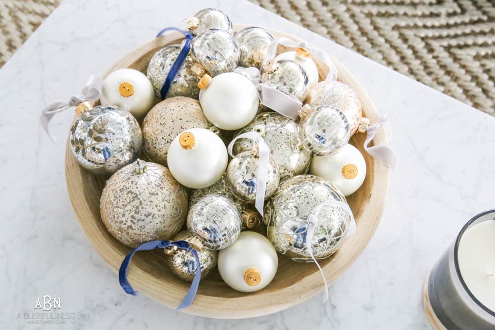 Mercury glass ornaments with velvet ribbons tied and collected in a wood bowl on a coffee table for a gorgeous holiday décor display. Simple touches for Christmas décor that make big impact. Check out all the white, silver and gold Christmas decor in this holiday home tour on ABlissfulNest.com. #ABlissfulNest #Christmasdecor #Christmasdecorating #CoastalChristmasdecor #christmastree #christmasmantle