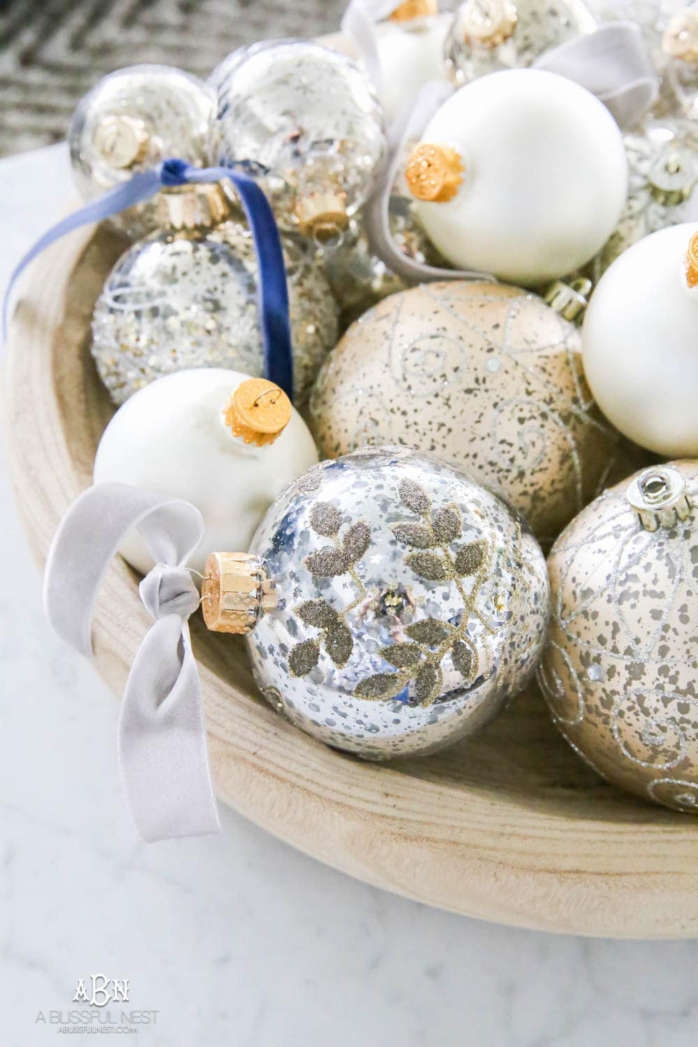 Mercury glass ornaments with velvet ribbons tied and collected in a wood bowl on a coffee table for a gorgeous holiday décor display. Simple touches for Christmas décor that make big impact. Check out all the white, silver and gold Christmas decor in this holiday home tour on ABlissfulNest.com. #ABlissfulNest #Christmasdecor #Christmasdecorating #CoastalChristmasdecor #christmastree #christmasmantle