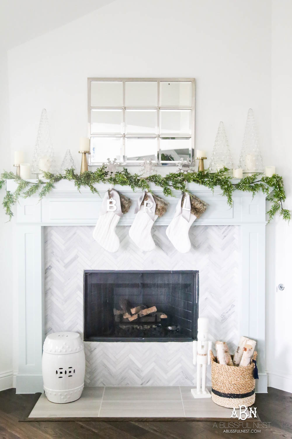 Gorgeous blue and silver Christmas mantle décor with juniper berry garland and glass hurricane Christmas trees. Simple and festive holiday décor in this open concept living space. Check out all the white, silver and gold Christmas decor in this holiday home tour on ABlissfulNest.com. #ABlissfulNest #Christmasdecor #Christmasdecorating #CoastalChristmasdecor #christmastree #christmasmantle