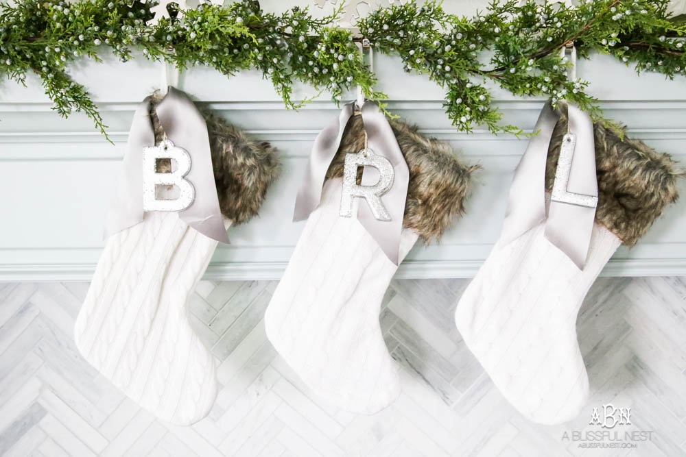 Gorgeous blue and silver Christmas mantle décor with juniper berry garland and glass hurricane Christmas trees. Simple and festive holiday décor in this open concept living space. Check out all the white, silver and gold Christmas decor in this holiday home tour on ABlissfulNest.com. #ABlissfulNest #Christmasdecor #Christmasdecorating #CoastalChristmasdecor #christmastree #christmasmantle