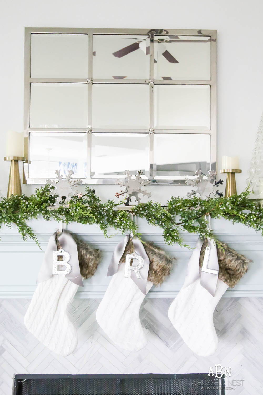 Gorgeous blue and silver Christmas mantle décor with juniper berry garland and glass hurricane Christmas trees. Simple and festive holiday décor in this open concept living space. Check out all the white, silver and gold Christmas decor in this holiday home tour on ABlissfulNest.com. #ABlissfulNest #Christmasdecor #Christmasdecorating #CoastalChristmasdecor #christmastree #christmasmantle