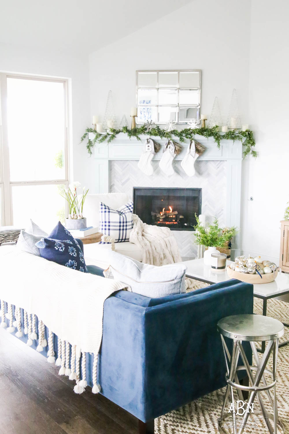 Gorgeous blue and silver Christmas mantle décor with juniper berry garland and glass hurricane Christmas trees. Simple and festive holiday décor in this open concept living space. Check out all the white, silver and gold Christmas decor in this holiday home tour on ABlissfulNest.com. #ABlissfulNest #Christmasdecor #Christmasdecorating #CoastalChristmasdecor #christmastree #christmasmantle