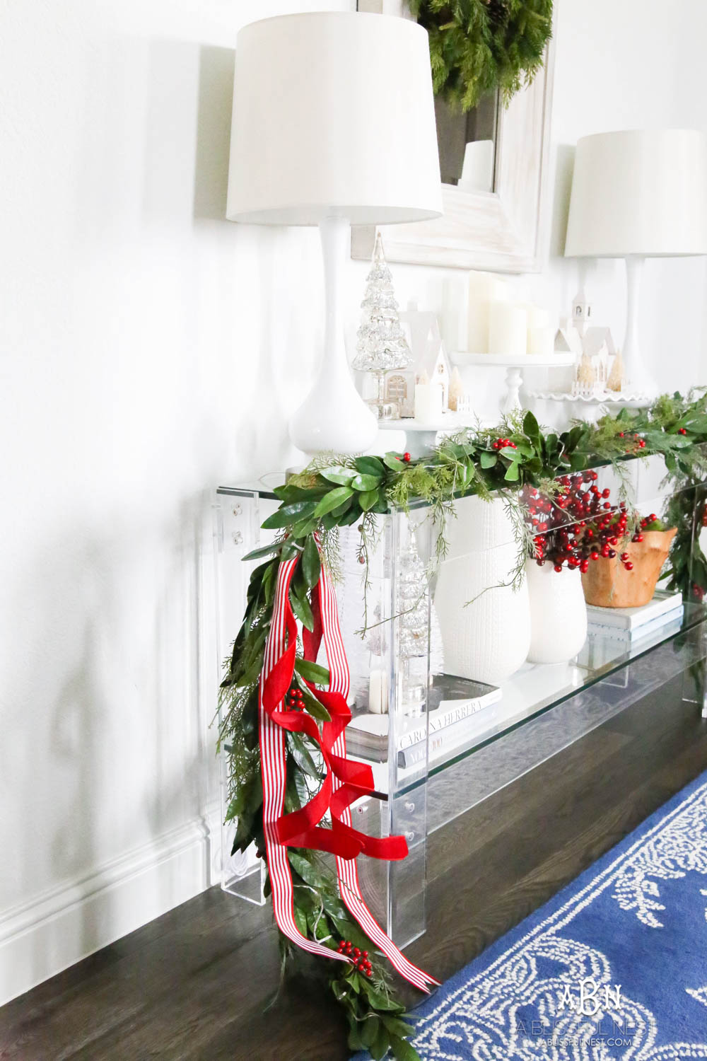 Layered garland makes a full look and adding in festive red and white ribbon. Love these easy and simple classic Christmas touches in this entryway. #christmasentryway #christmasentry #christmasentrydecor #christmasentrywayideas #christmashometour