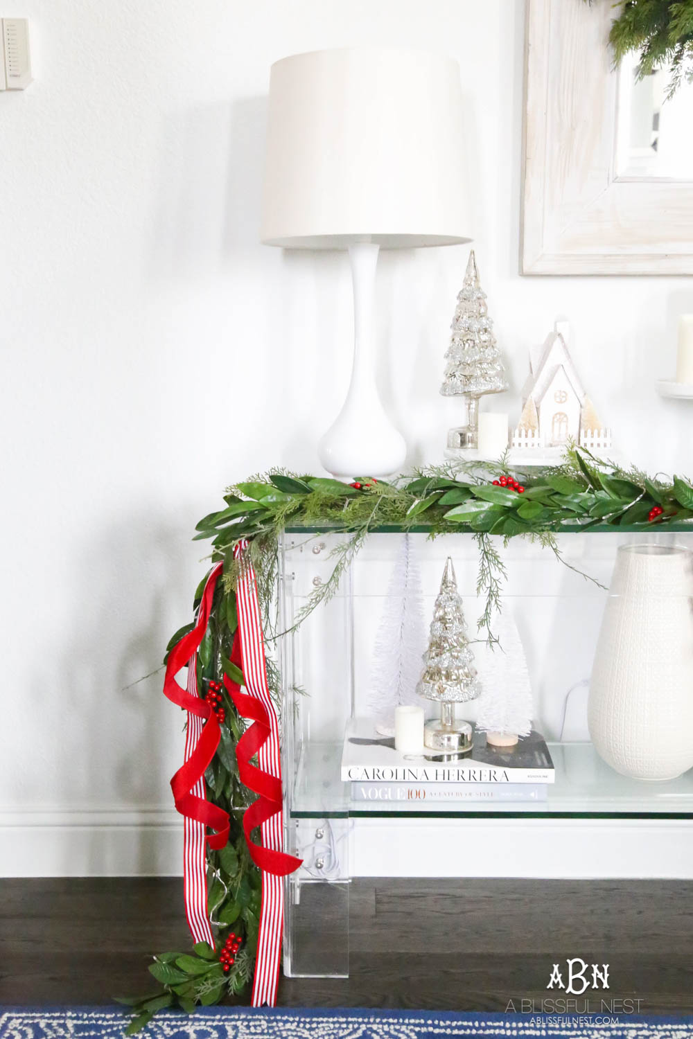 Create a display with your mini trees by clustering them on top of décor books and adding in candles. More ways to add in classic Christmas décor into your home on ablissfulnest.com. #christmasentryway #christmasentry #christmasentrydecor #christmasentrywayideas #christmashometour