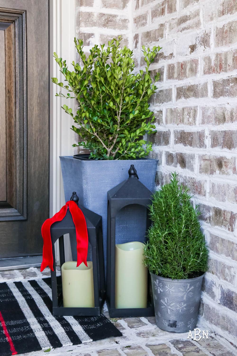 Classic Christmas front porch with red, white and black details. Festive plaid door mat and simple black lanterns. Red Christmas balls on a beautiful Christmas wreath. #christmasporch #christmasfrontporch #christmasporchdecor #christmasporchideas #christmashometou