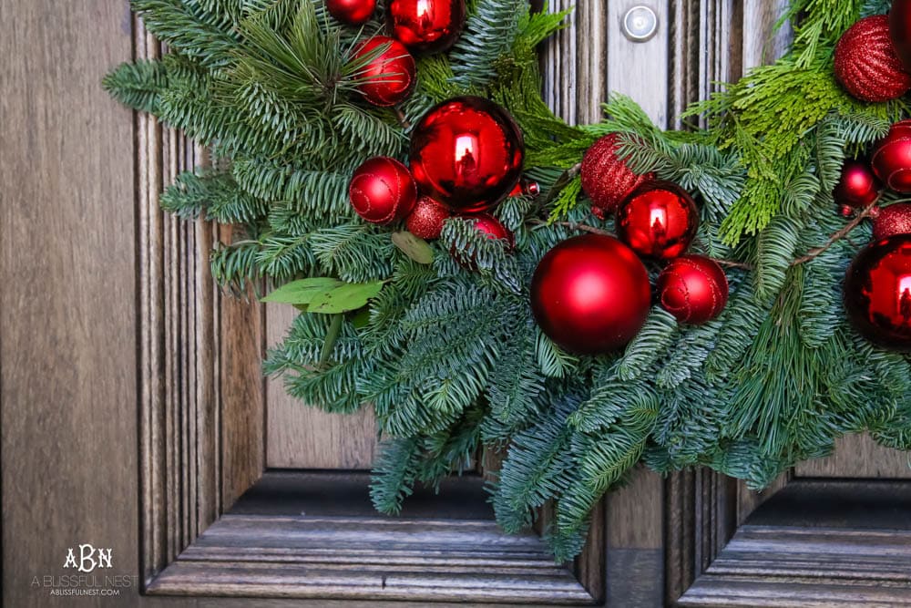 Classic Christmas front porch with red, white and black details. Festive plaid door mat and simple black lanterns. Red Christmas balls on a beautiful Christmas wreath. #christmasporch #christmasfrontporch #christmasporchdecor #christmasporchideas #christmashometou