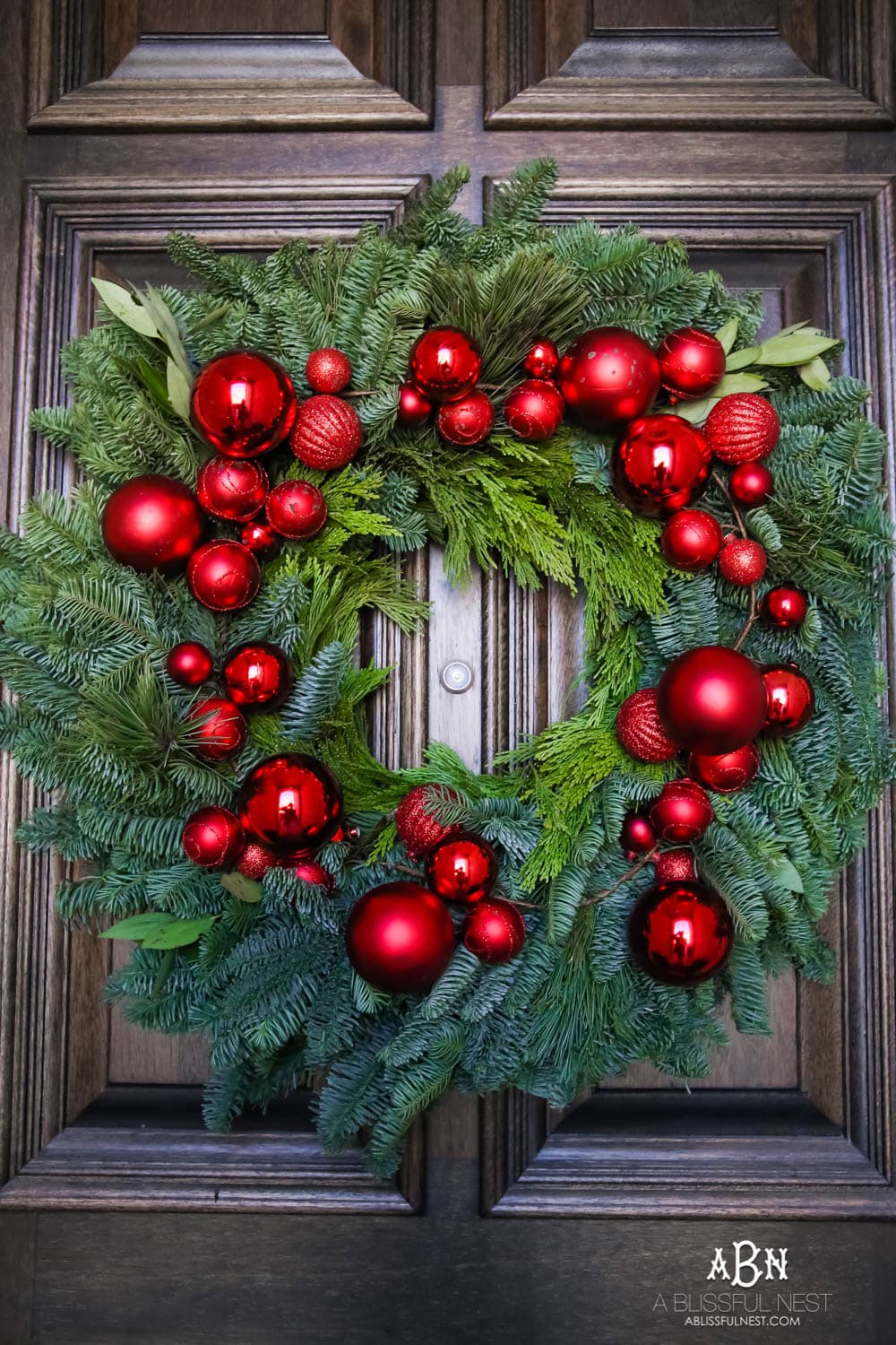 Classic Christmas front porch with red, white and black details. Festive plaid door mat and simple black lanterns. Red Christmas balls on a beautiful Christmas wreath. #christmasporch #christmasfrontporch #christmasporchdecor #christmasporchideas #christmashometou