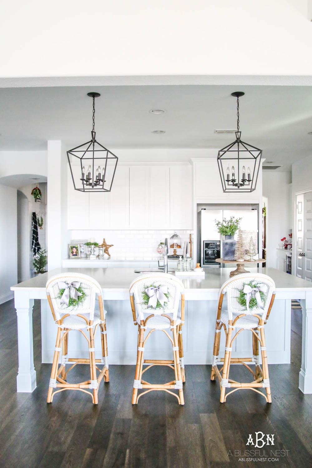 Blue and silver Christmas kitchen décor. All white kitchen with subtle holiday décor for a fresh coastal Christmas look. Mini wreaths on the backs of the barstools, beautiful bay leaf above the range. #christmaskitchen #christmashometour #holidayhometour #kitchenideas