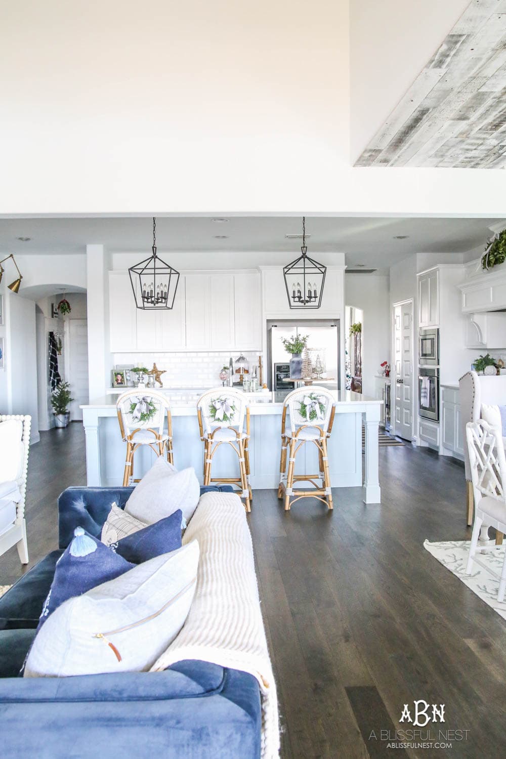 Blue and silver Christmas kitchen décor. All white kitchen with subtle holiday décor for a fresh coastal Christmas look. Mini wreaths on the backs of the barstools, beautiful bay leaf above the range. #christmaskitchen #christmashometour #holidayhometour #kitchenideas