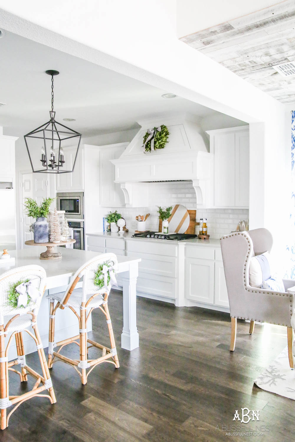 Blue and silver Christmas kitchen décor. All white kitchen with subtle holiday décor for a fresh coastal Christmas look. Mini wreaths on the backs of the barstools, beautiful bay leaf above the range. #christmaskitchen #christmashometour #holidayhometour #kitchenideas