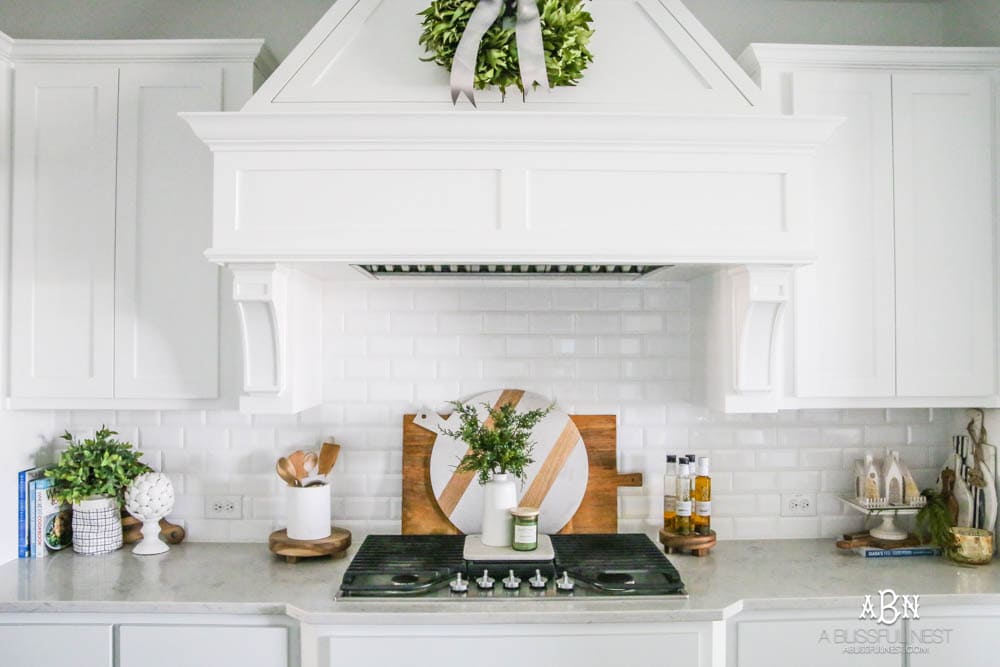 Blue and silver Christmas kitchen décor. All white kitchen with subtle holiday décor for a fresh coastal Christmas look. Mini wreaths on the backs of the barstools, beautiful bay leaf above the range. #christmaskitchen #christmashometour #holidayhometour #kitchenideas