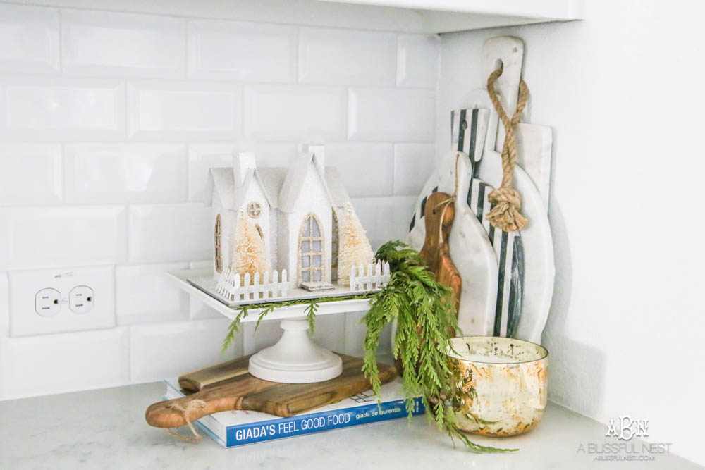 Blue and silver Christmas kitchen décor. All white kitchen with subtle holiday décor for a fresh coastal Christmas look. Mini wreaths on the backs of the barstools, beautiful bay leaf above the range. #christmaskitchen #christmashometour #holidayhometour #kitchenideas