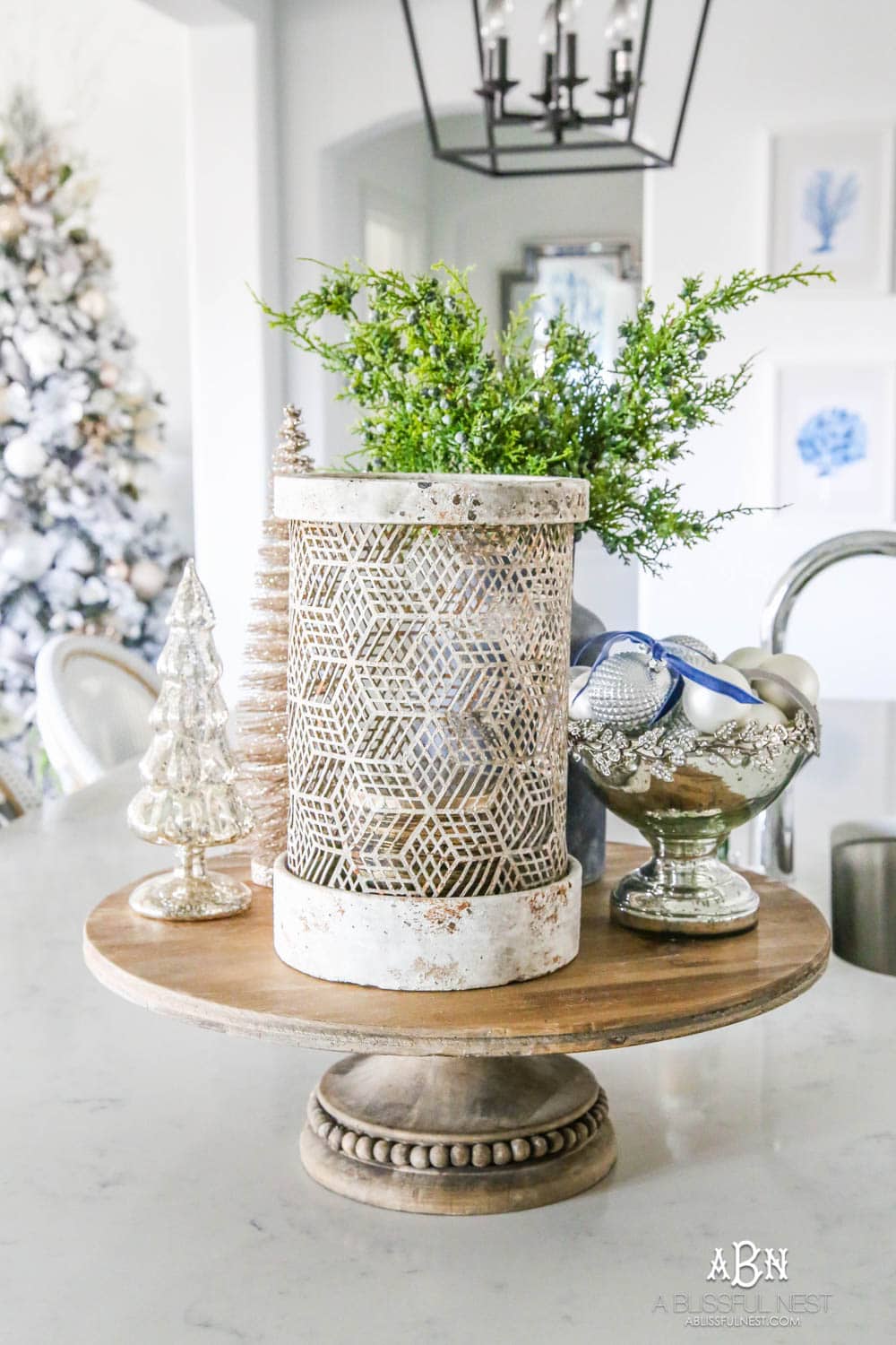 Blue and silver Christmas kitchen décor. All white kitchen with subtle holiday décor for a fresh coastal Christmas look. Mini wreaths on the backs of the barstools, beautiful bay leaf above the range. #christmaskitchen #christmashometour #holidayhometour #kitchenideas