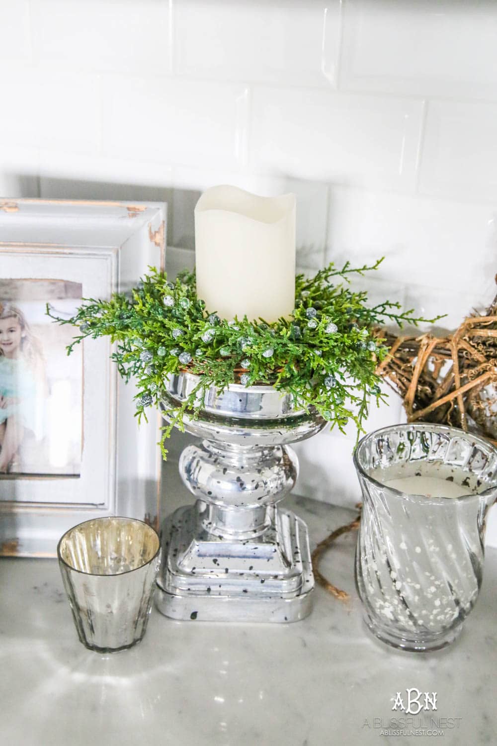 Blue and silver Christmas kitchen décor. All white kitchen with subtle holiday décor for a fresh coastal Christmas look. Mini wreaths on the backs of the barstools, beautiful bay leaf above the range. #christmaskitchen #christmashometour #holidayhometour #kitchenideas