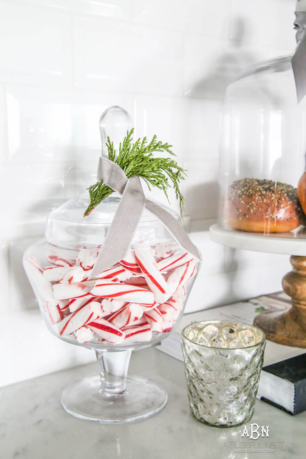 Blue and silver Christmas kitchen décor. All white kitchen with subtle holiday décor for a fresh coastal Christmas look. Mini wreaths on the backs of the barstools, beautiful bay leaf above the range. #christmaskitchen #christmashometour #holidayhometour #kitchenideas