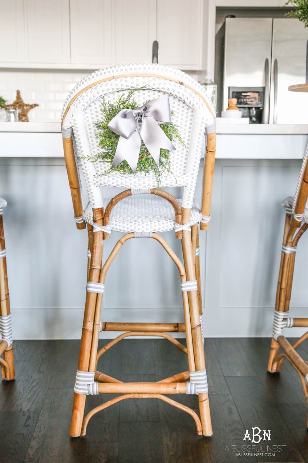 Blue and silver Christmas kitchen décor. All white kitchen with subtle holiday décor for a fresh coastal Christmas look. Mini wreaths on the backs of the barstools, beautiful bay leaf above the range. #christmaskitchen #christmashometour #holidayhometour #kitchenideas