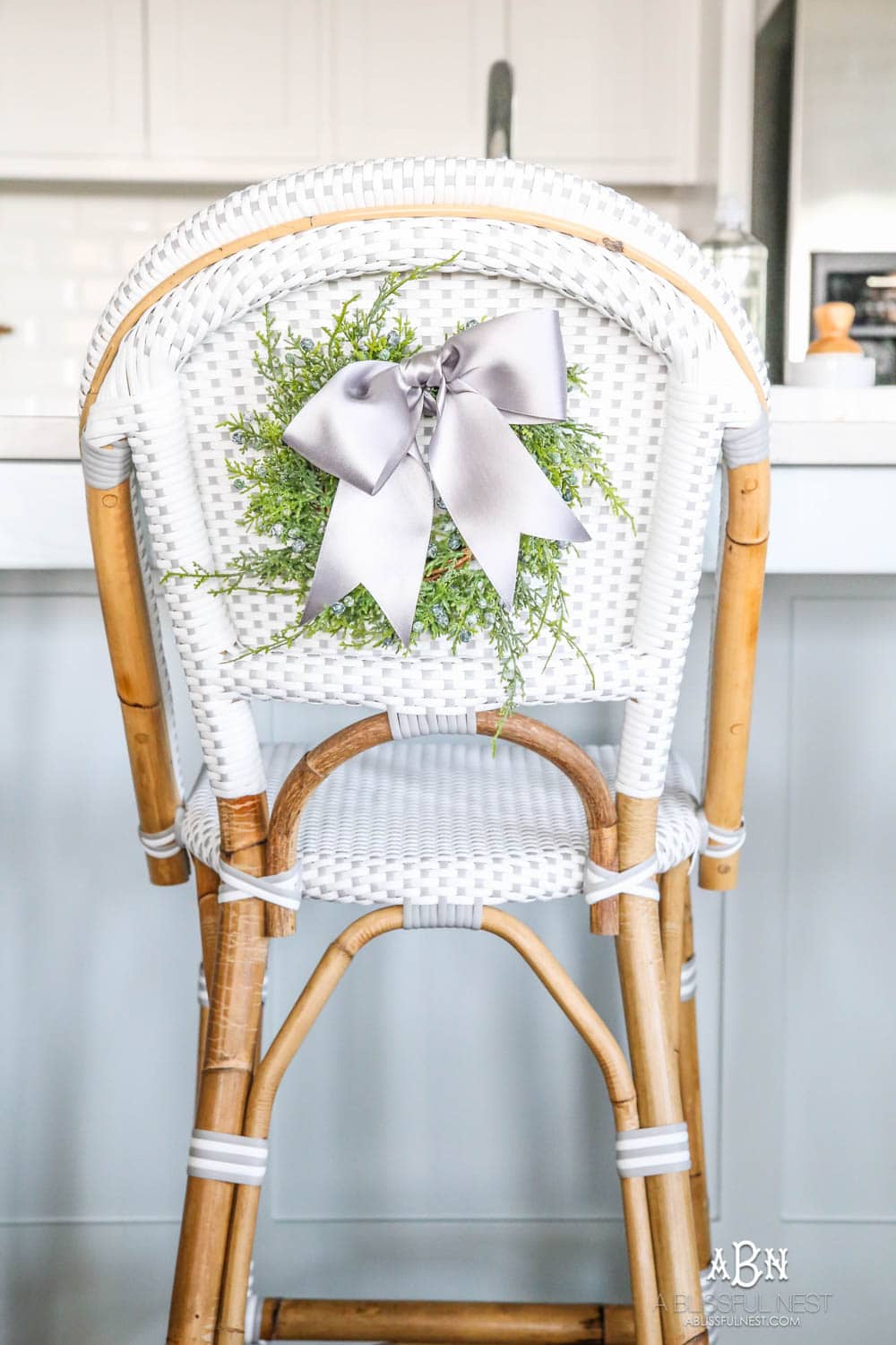 Blue and silver Christmas kitchen décor. All white kitchen with subtle holiday décor for a fresh coastal Christmas look. Mini wreaths on the backs of the barstools, beautiful bay leaf above the range. #christmaskitchen #christmashometour #holidayhometour #kitchenideas