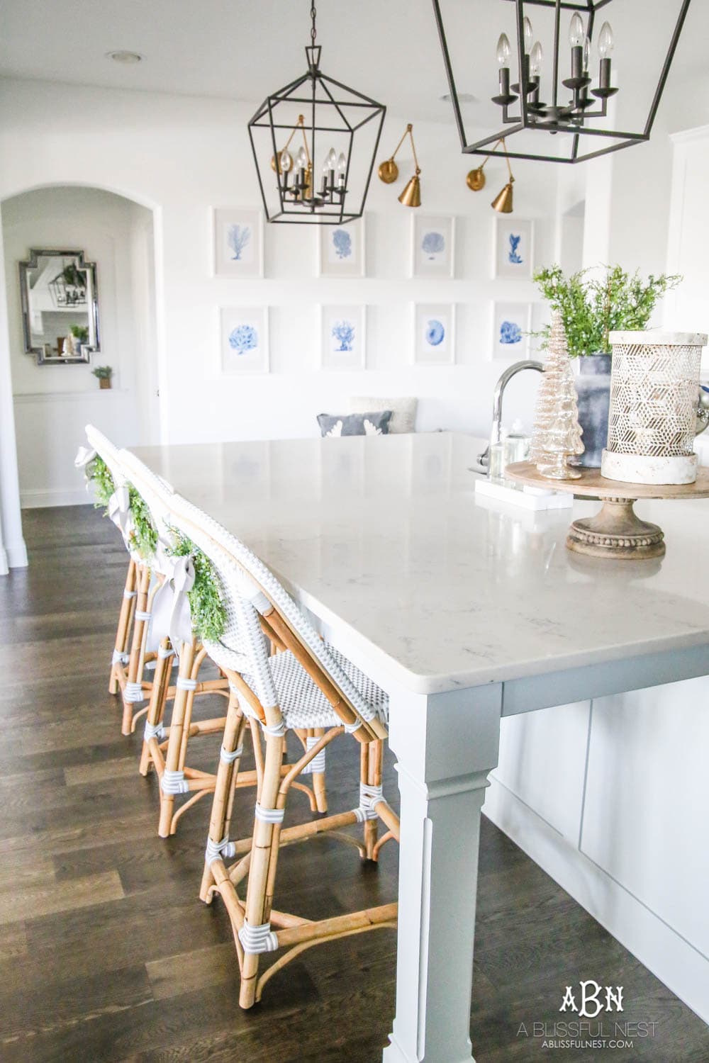 Blue and silver Christmas kitchen décor. All white kitchen with subtle holiday décor for a fresh coastal Christmas look. Mini wreaths on the backs of the barstools, beautiful bay leaf above the range. #christmaskitchen #christmashometour #holidayhometour #kitchenideas