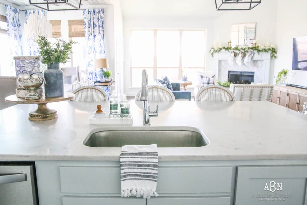 Blue and silver Christmas kitchen décor. All white kitchen with subtle holiday décor for a fresh coastal Christmas look. Mini wreaths on the backs of the barstools, beautiful bay leaf above the range. #christmaskitchen #christmashometour #holidayhometour #kitchenideas