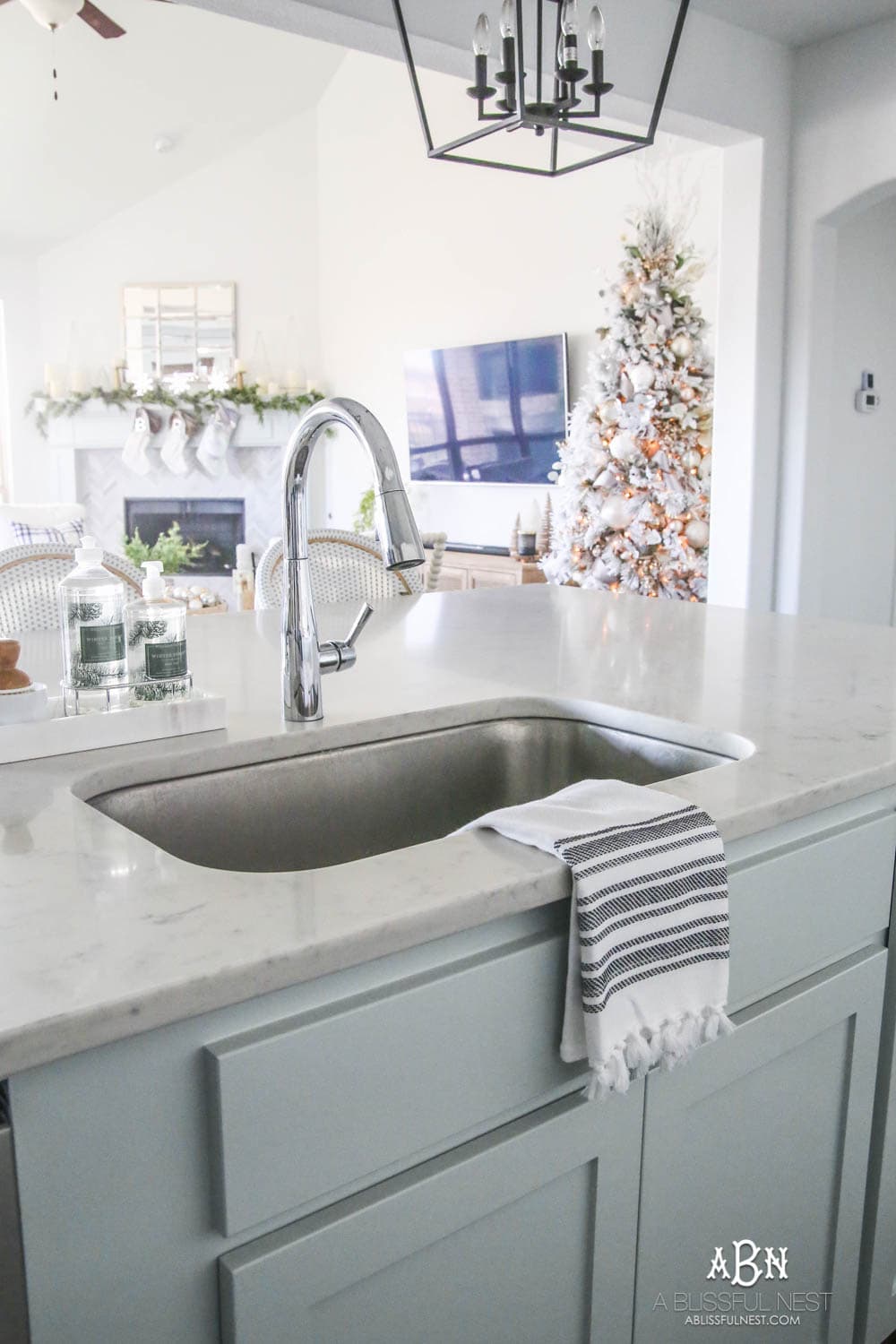 Blue and silver Christmas kitchen décor. All white kitchen with subtle holiday décor for a fresh coastal Christmas look. Mini wreaths on the backs of the barstools, beautiful bay leaf above the range. #christmaskitchen #christmashometour #holidayhometour #kitchenideas