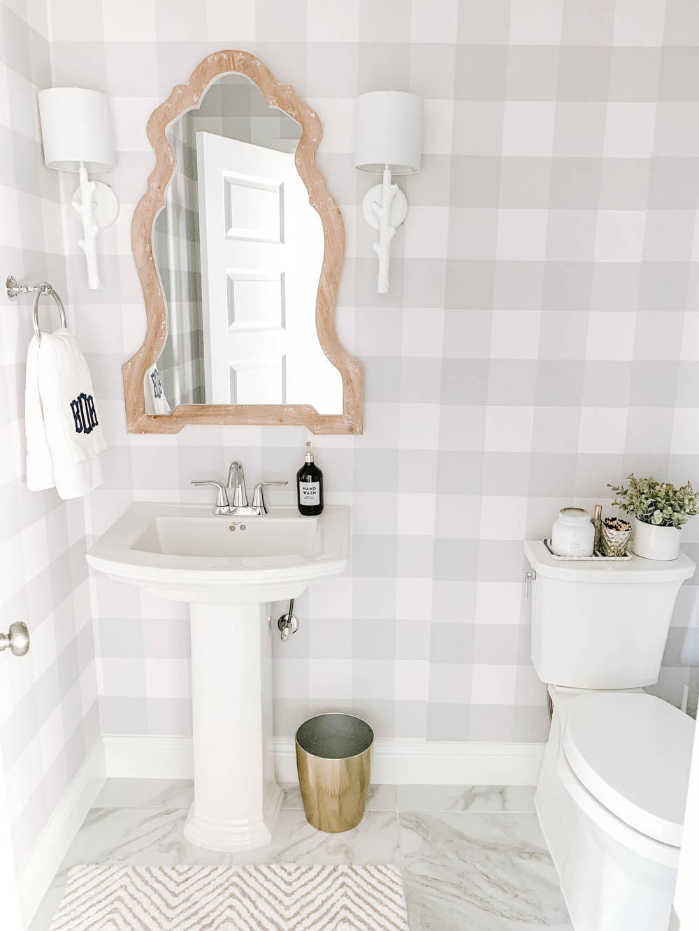 This farmhouse bathroom features grey and white buffalo check wallpaper, gold accents and a white washed wood mirror. #ABlissfulNest #bathroom #bathroomdesign #farmhouse #powderbathroom