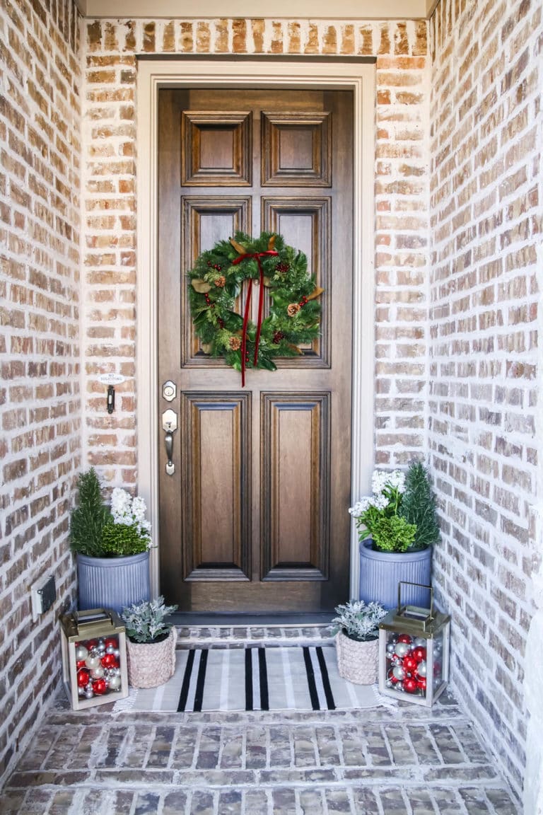 A traditional Christmas porch in red and green with gold lanterns, Christmas ornaments and fresh flowers. #ABlissfulNest #christmasporch #christmasdecorating