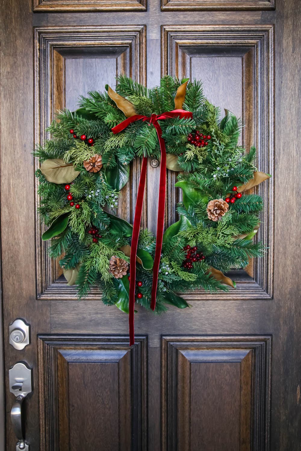 A beautiful traditional wreath with a velvet red ribbon, pincones and magnolia leaves. #ABlissfulNest #christmasporch #christmasdecorating