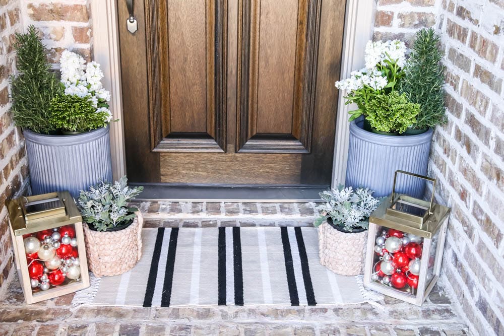 Gold lantern filled with Christmas ornaments, fresh winter flowers and a striped doormat. #ABlissfulNest #christmasporch #christmasdecor