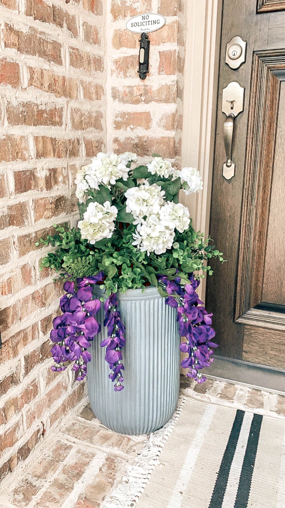 Outdoor planter on front porch filled with faux UV protected faux flowers. 