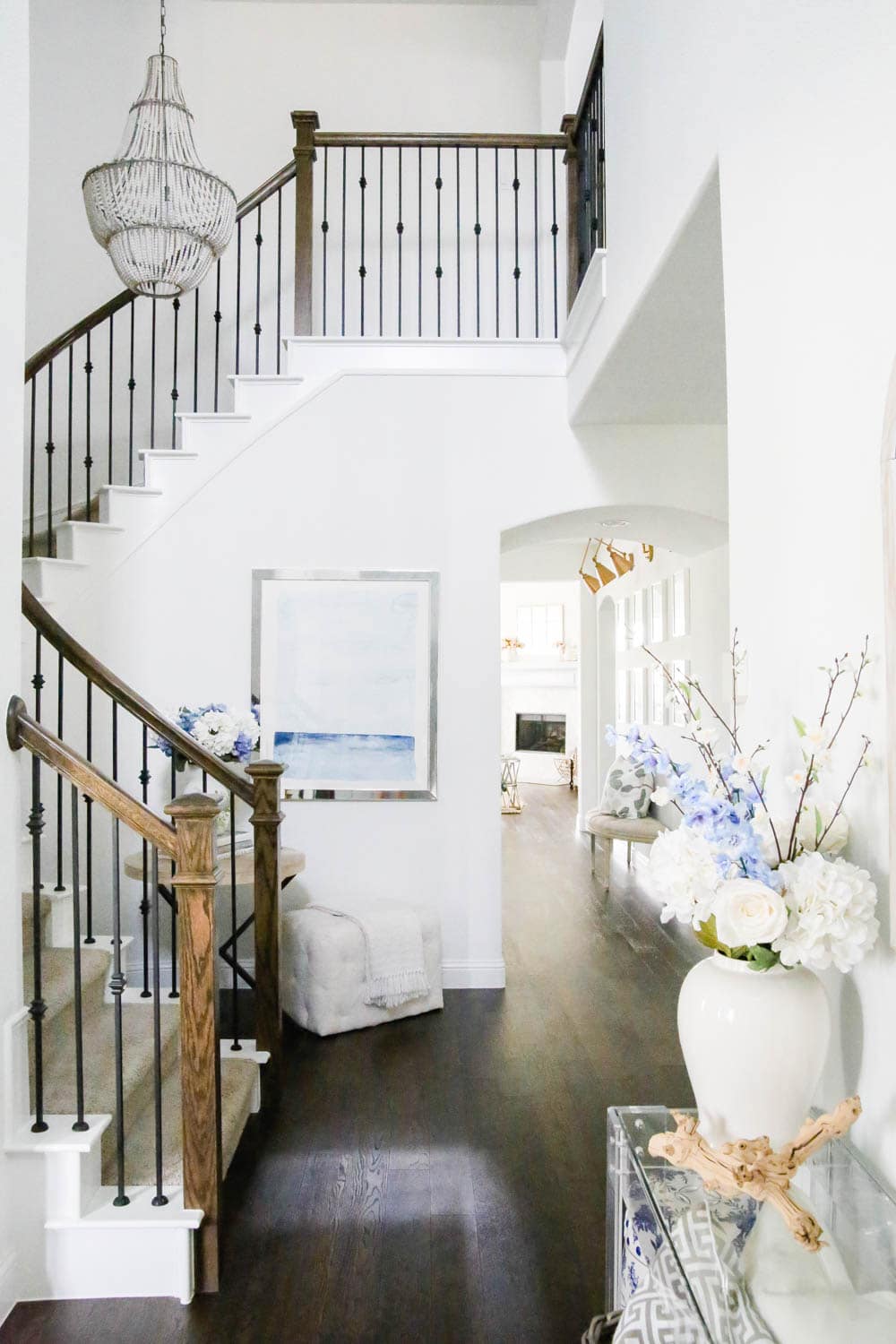 Entryway view with blue and white decor, ocean art, beaded chandelier, flowers in white vase, white painted interior. #ABlissfulNest #entrydecor #entryway #designtips