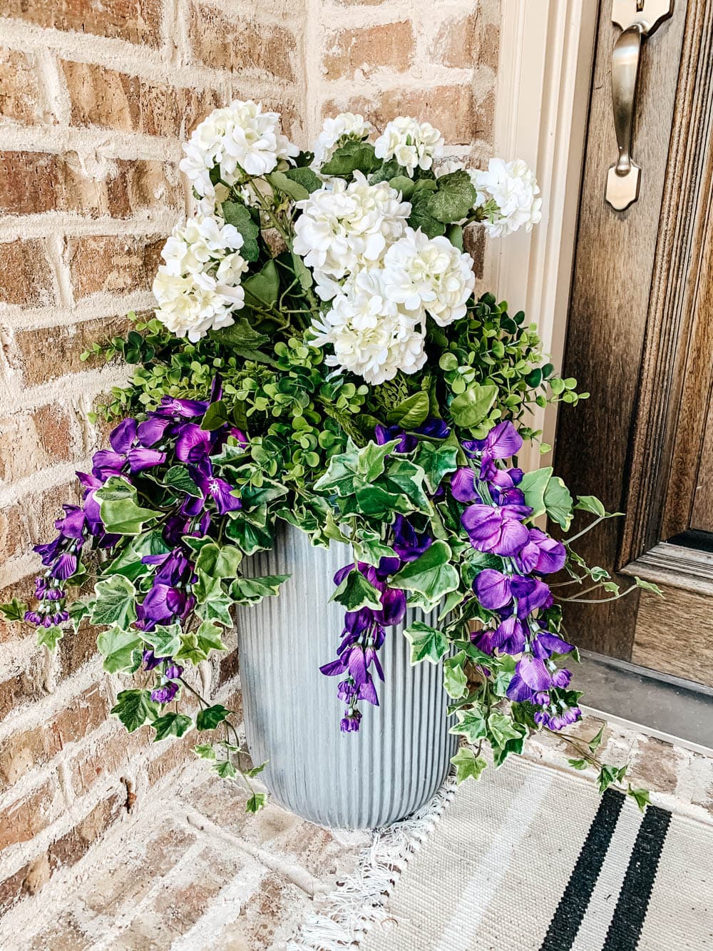 Tall grey fluted planter filled with faux ivy and white geraniums.