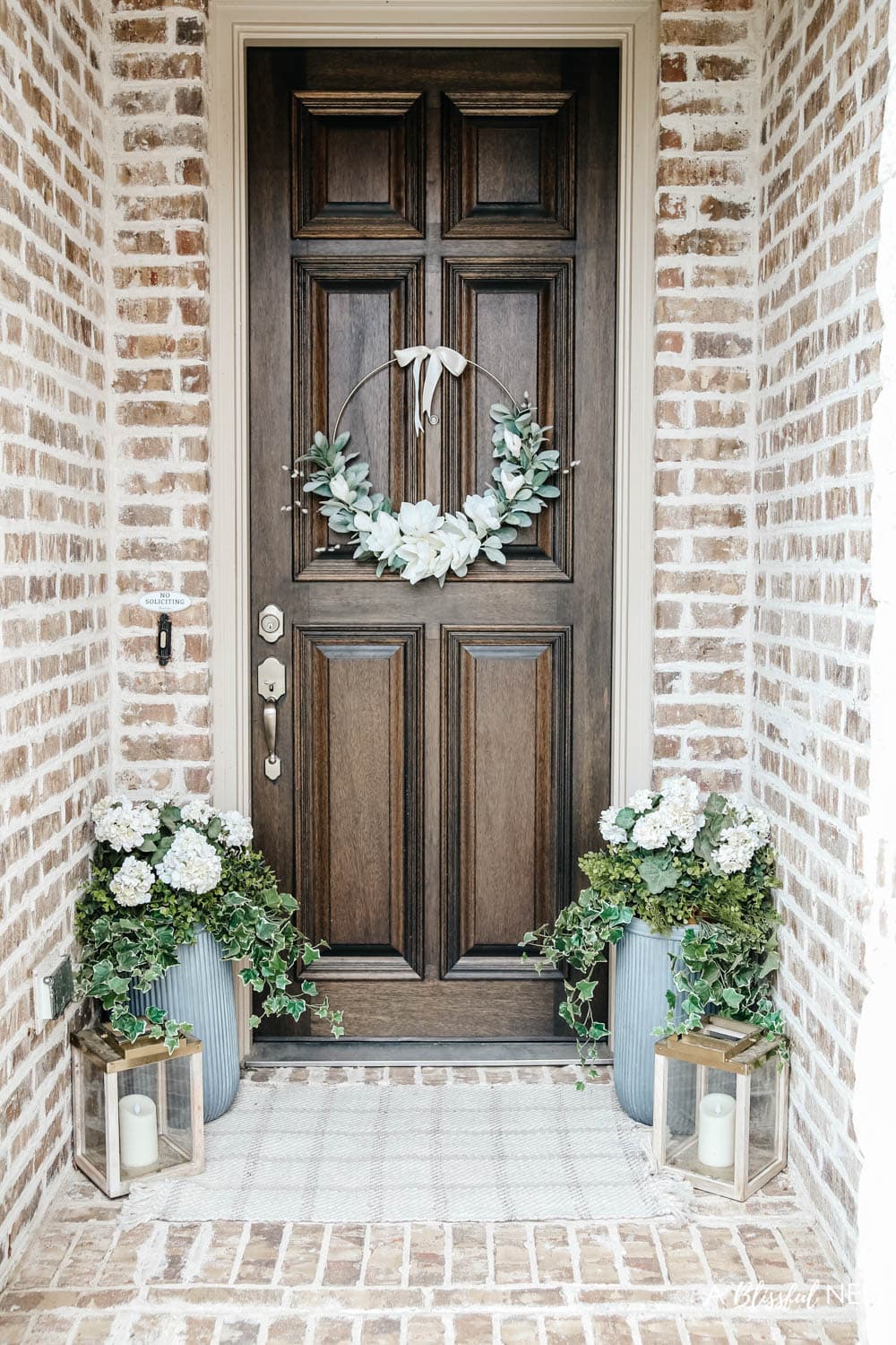 A simple fresh summer porch includes this beautiful hoop wreath, UV protected outdoor faux flowers, lanterns and more. #ABlissfulNest #summerporch #summerdecor