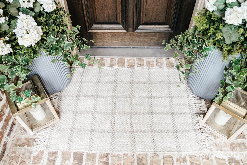 A simple fresh summer porch includes this beautiful hoop wreath, UV protected outdoor faux flowers, lanterns and more. #ABlissfulNest #summerporch #summerdecor