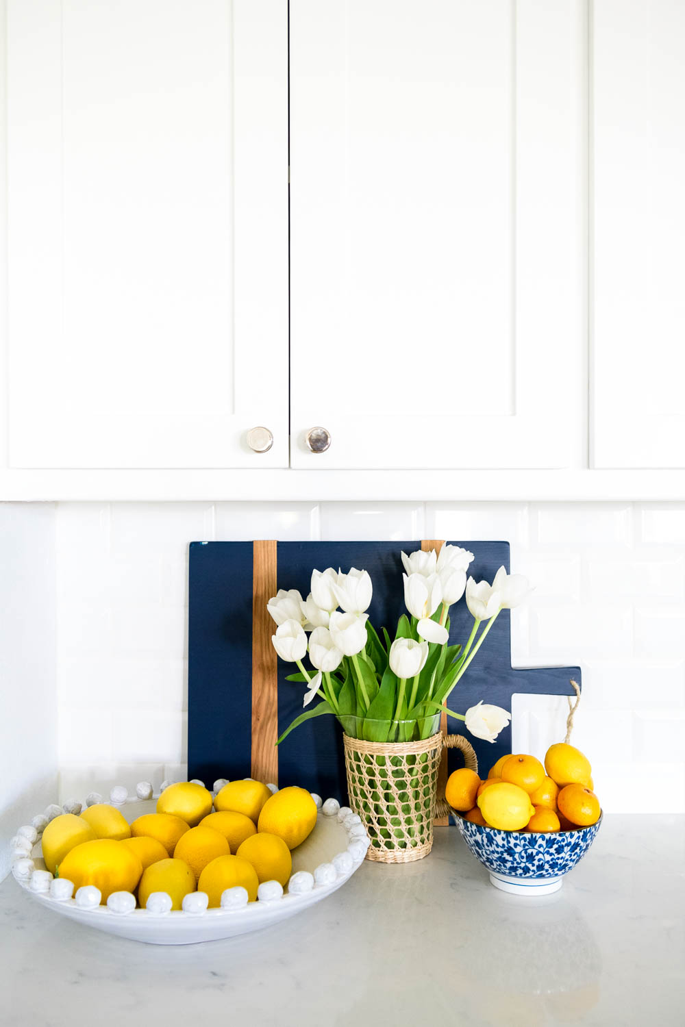 Add a bowl of fruit for color, blue and white bowl, tulips, cutting boards. #ABlissfulNest #kitchendecor #whitekitchen