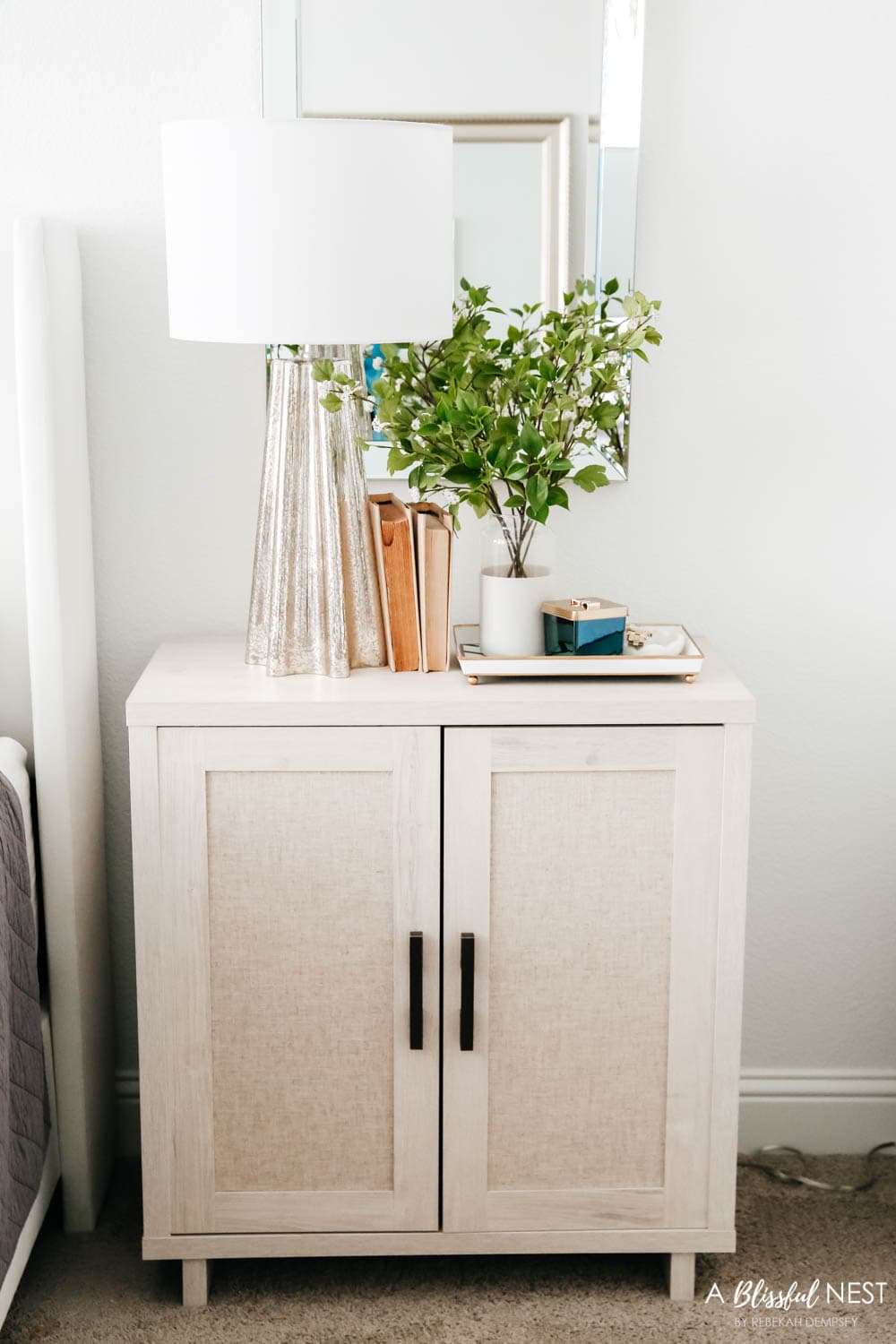 Nightstand with a silver table lamp and vintage books, vase with greenery.