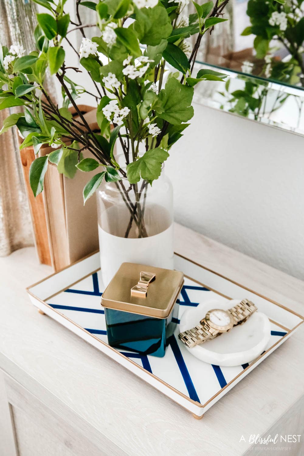 Nightstand with a silver table lamp and vintage books, vase with greenery.