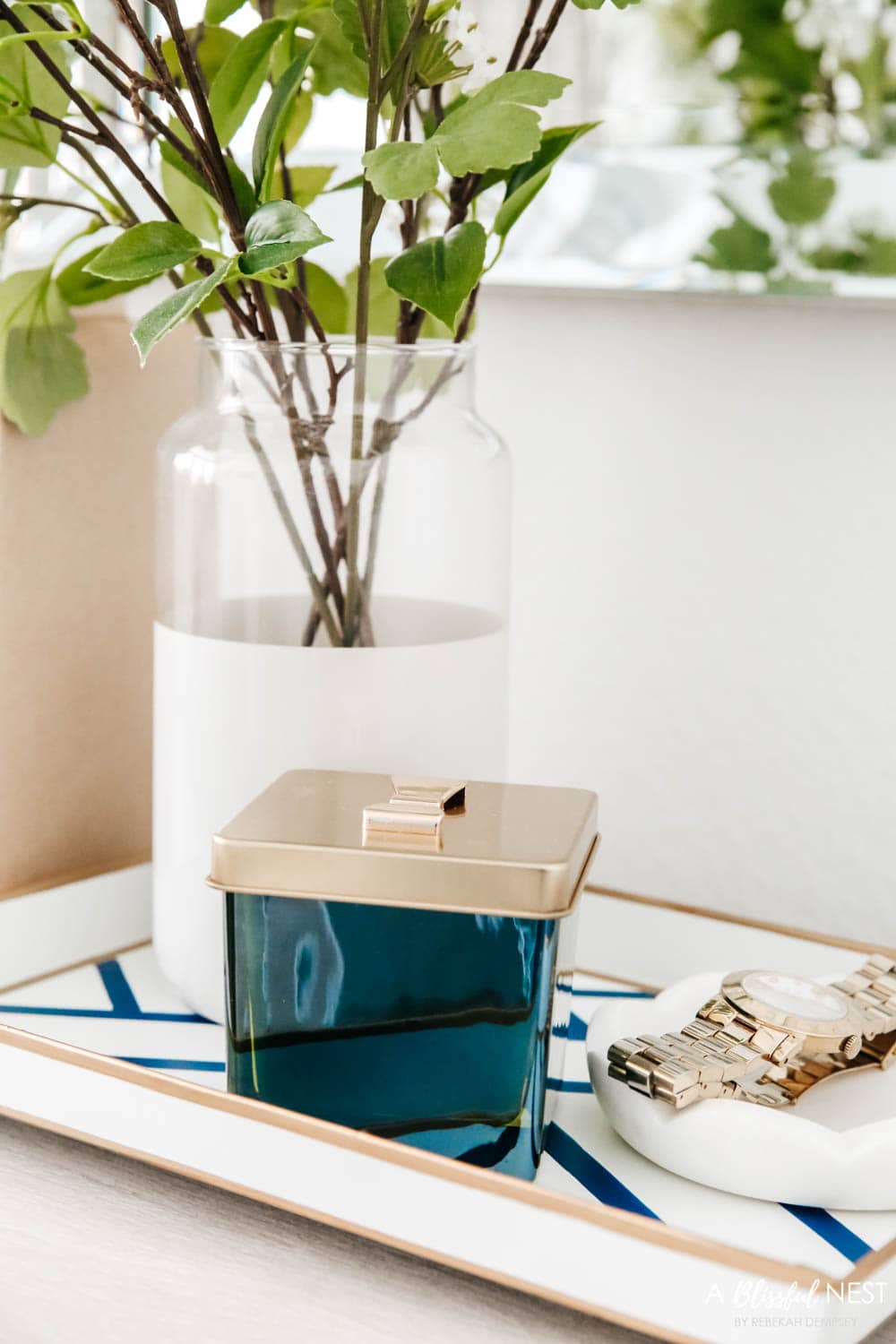 Nightstand with a silver table lamp and vintage books, vase with greenery.