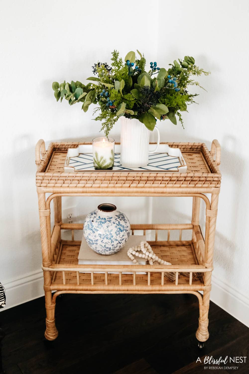 Rattan bar cart with holiday greenery, stack of books, blue and white vase, and wood bead garland.