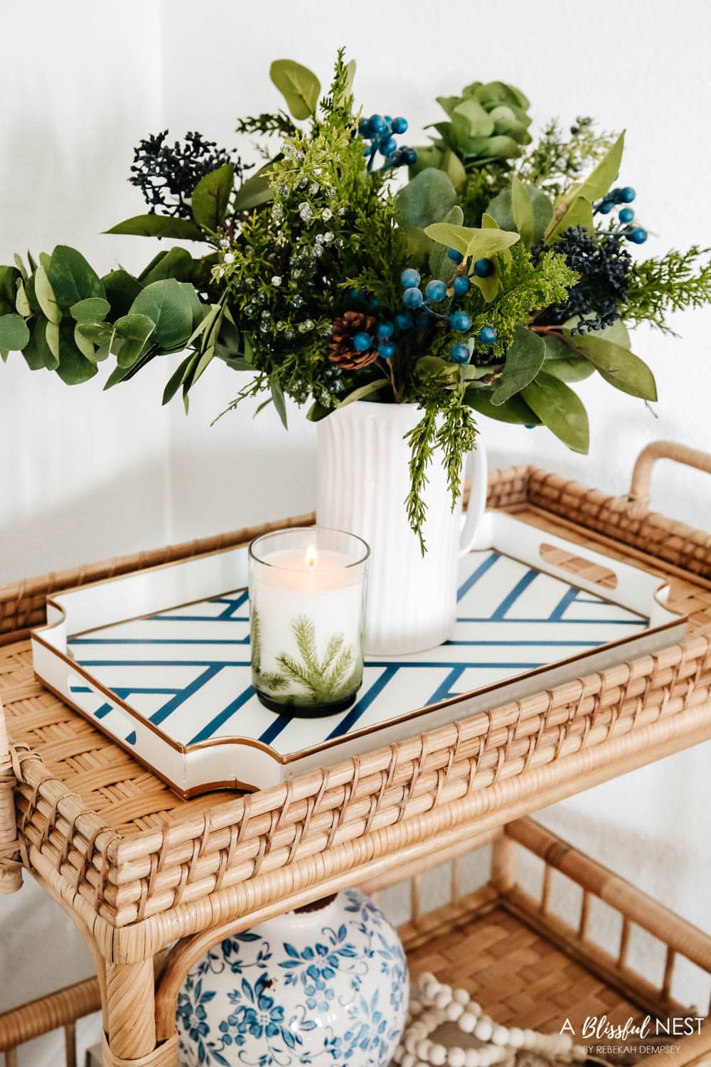 Rattan bar cart with holiday greenery, stack of books, blue and white vase, and wood bead garland.